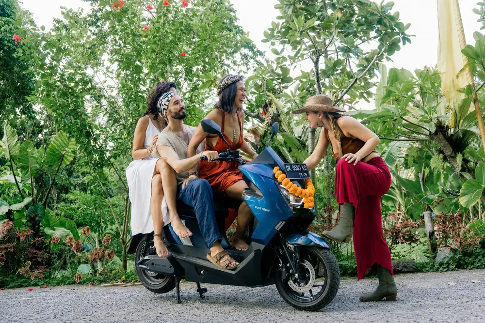 Four friends laughing around a blue electric motorbike in a Bali garden