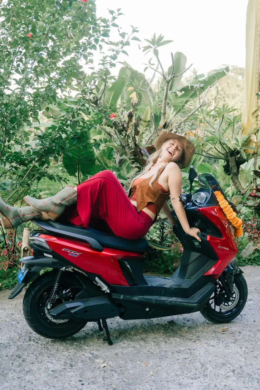 Rider laughing on a red electric motorbike in a tropical garden